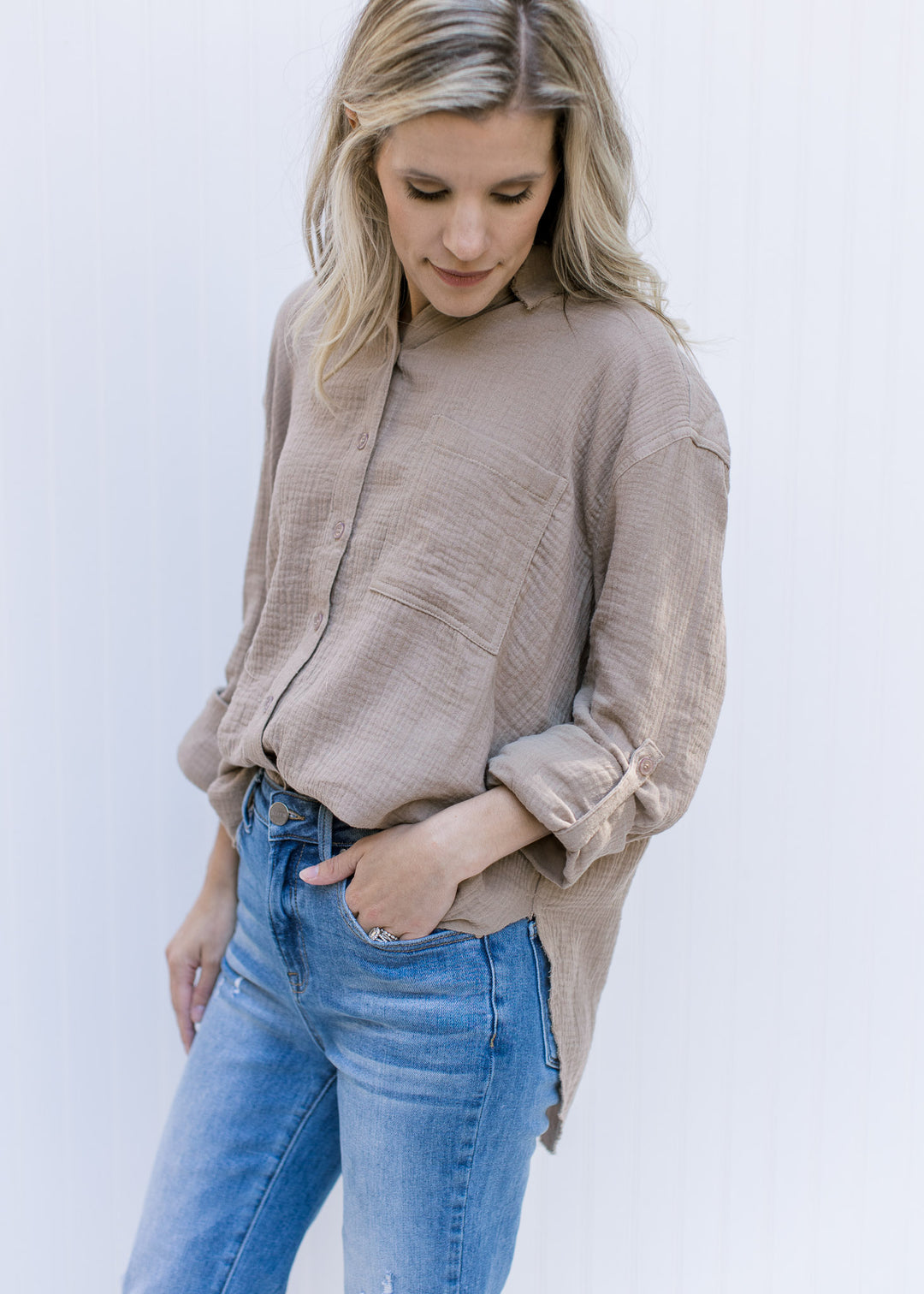Model wearing a taupe button up top with a raw hemline, a cotton gauze material and long sleeves.