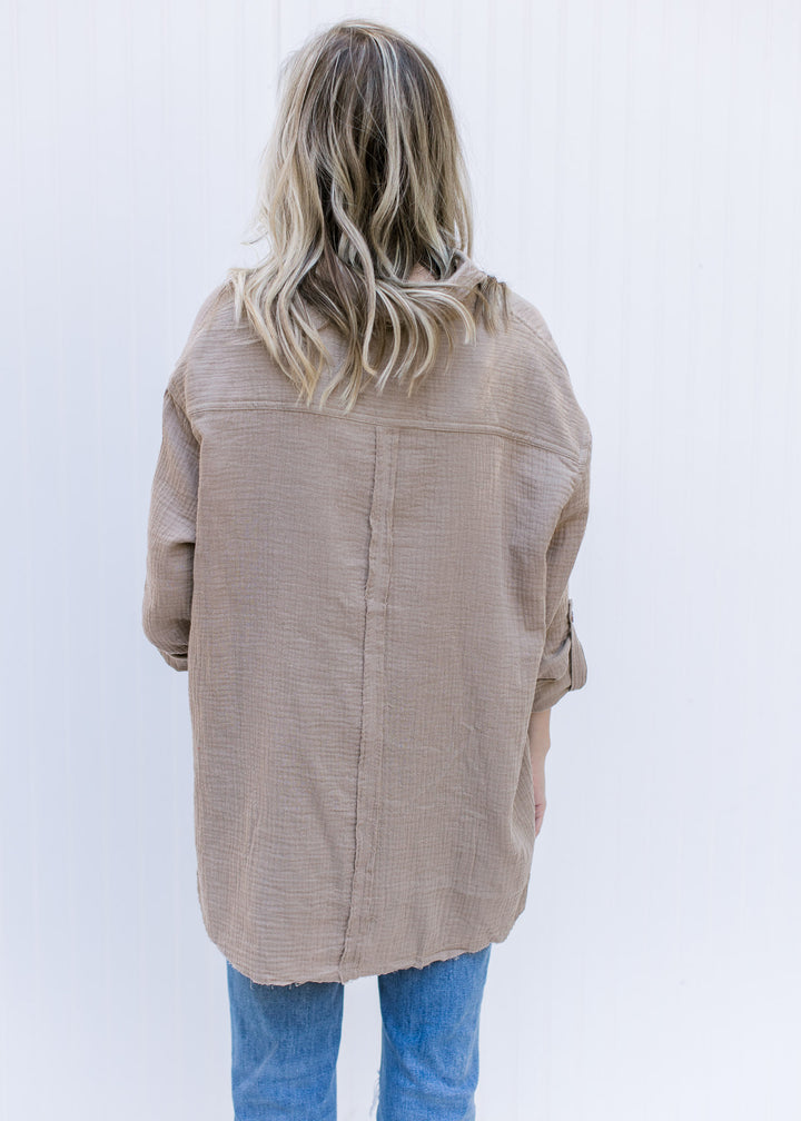 Back view of Model wearing a taupe long sleeve button up top with a raw hemline and cotton gauze.