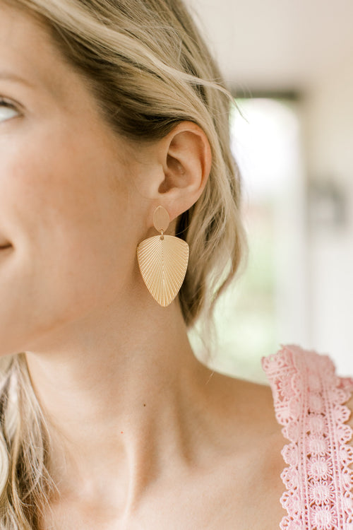 Model wearing elegant golden palm leaf-shaped dangle earrings. 