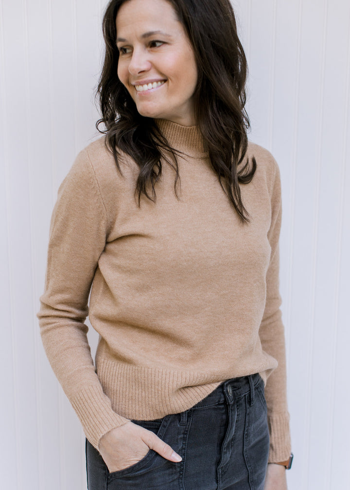 Model wearing jeans with a classic camel colored top with a mocked neckline and long sleeves.