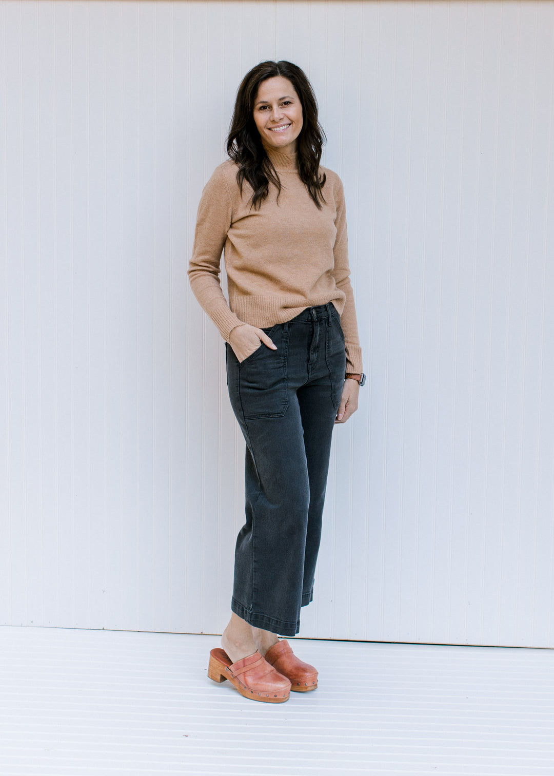 Model wearing jeans and mules with a camel colored top with a mocked neckline and long sleeves.