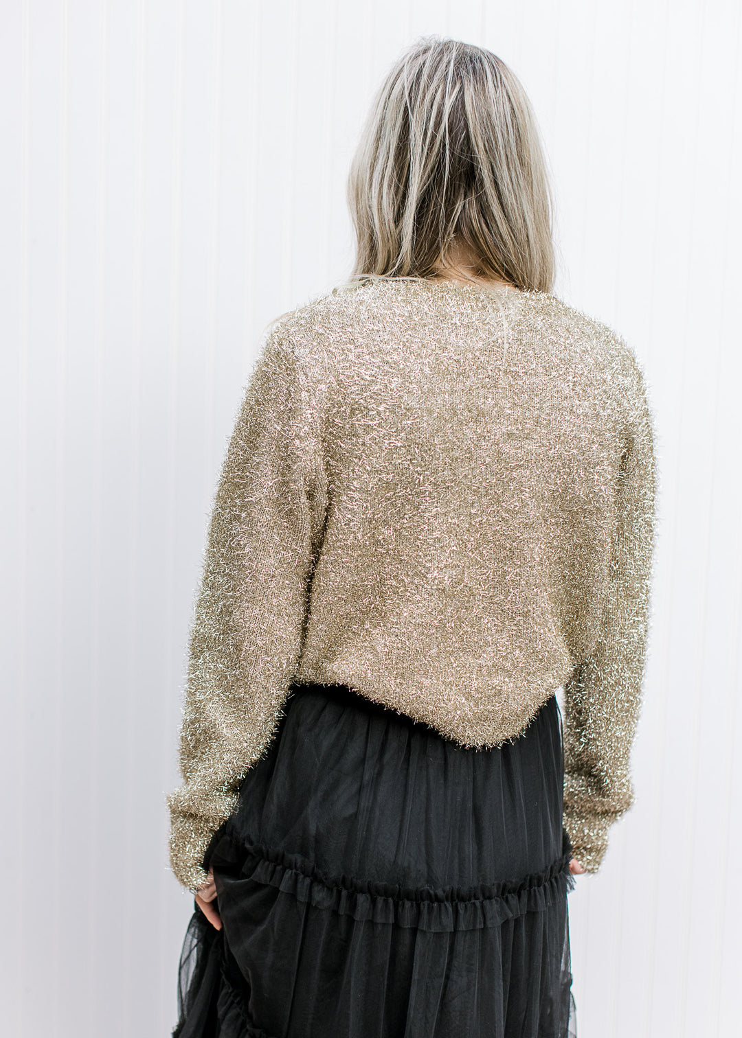Back view of  Model wearing a gold sweater with a tinsel material, round neck and long sleeves.