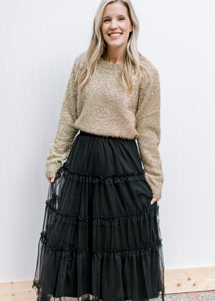 Model wearing a black skirt and a gold sweater with a tinsel material, round neck and long sleeves.