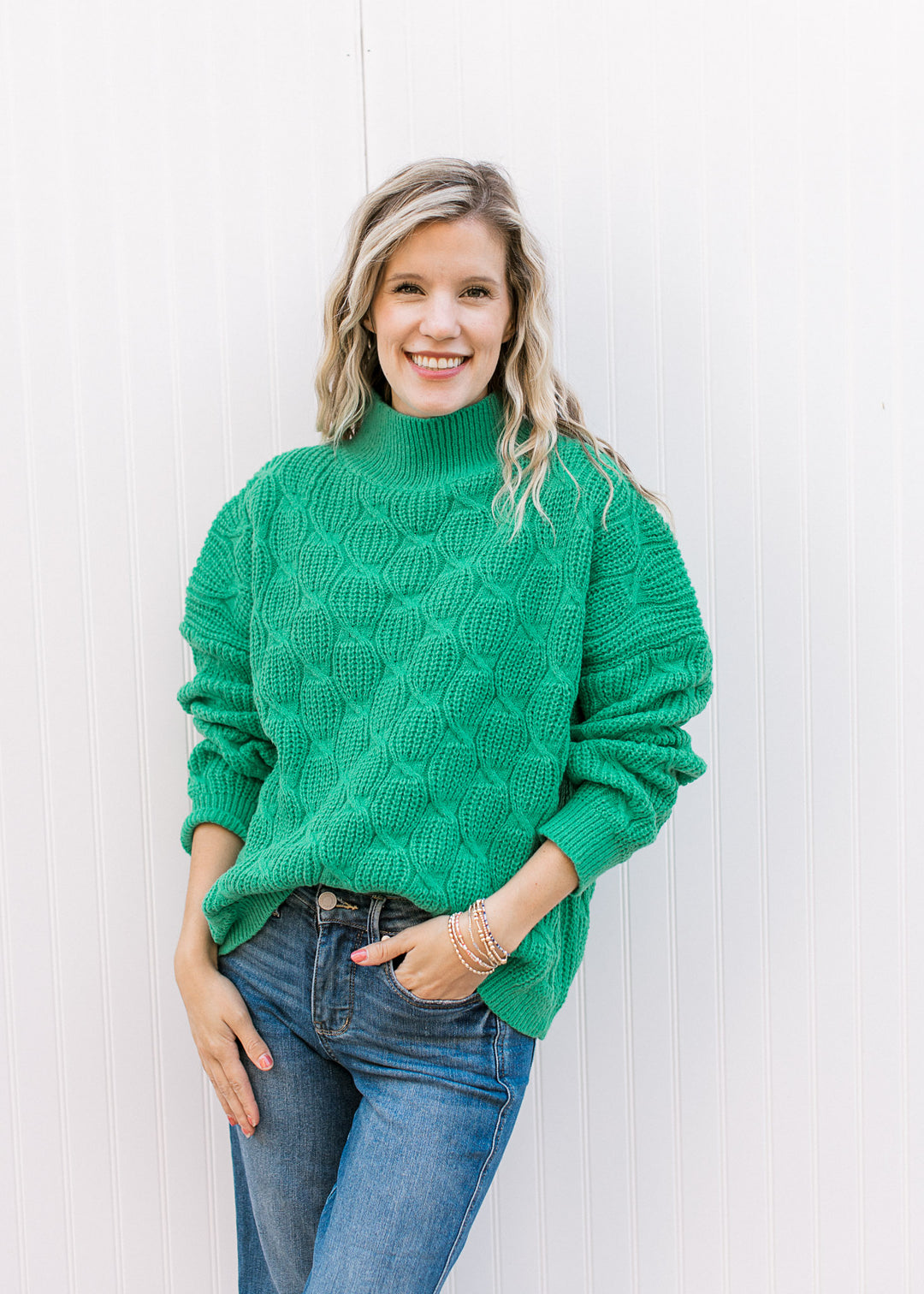 Model wearing a green long sleeve, cable knit sweater with ribbed mock neck, cuffs, and waist.