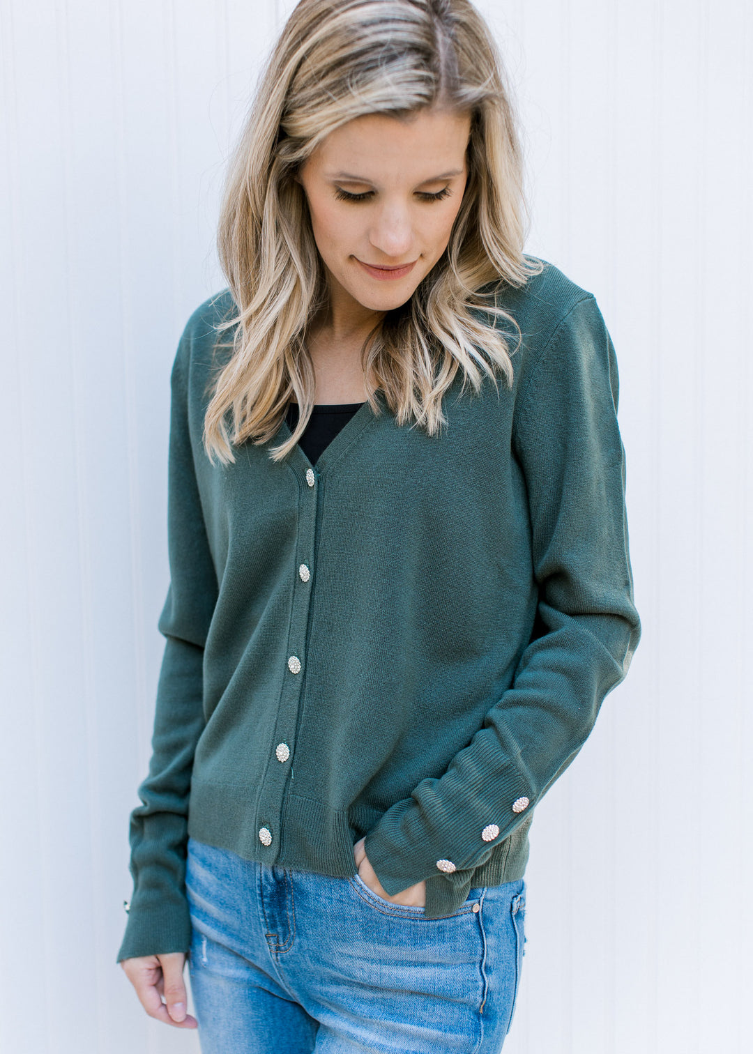 Model wearing jeans and a black top under a green long sleeve cardigan with flower rhinestone button