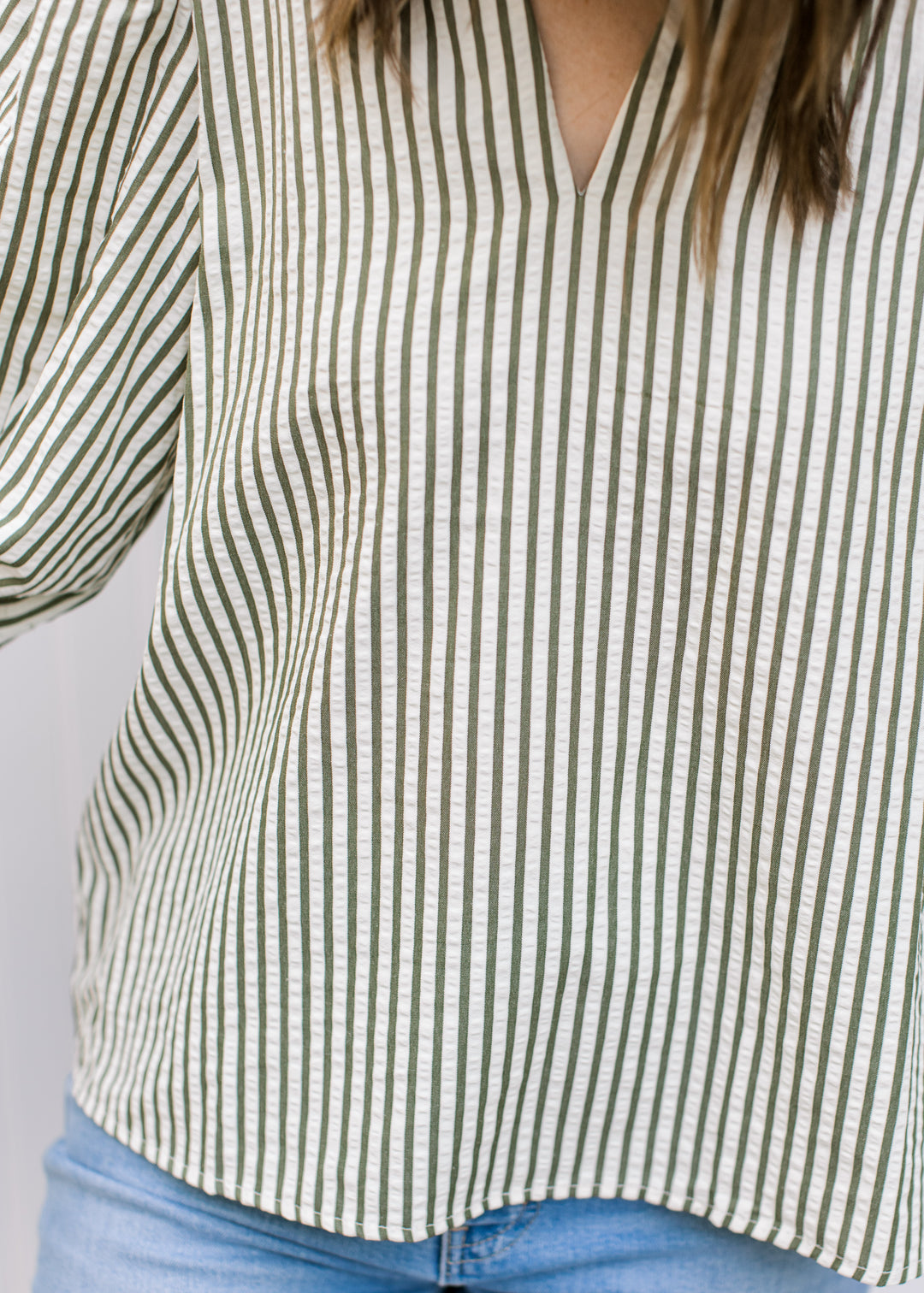 Close up of model wearing a cream top with green stripes, v-neck and 3/4 sleeve.