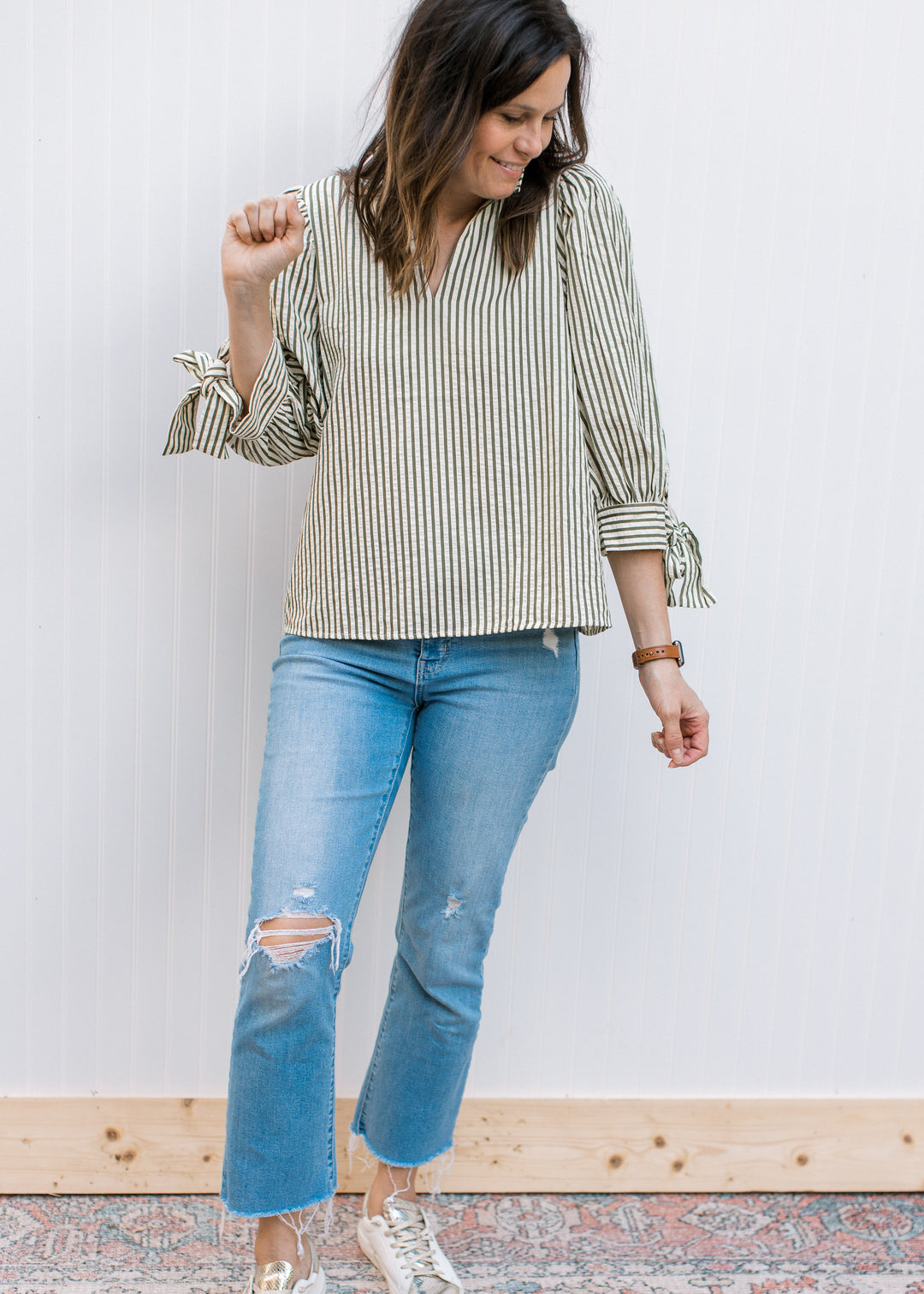 Model wearing jeans, sneakers and a cream v-neck top with green stripes, and 3/4 sleeves.