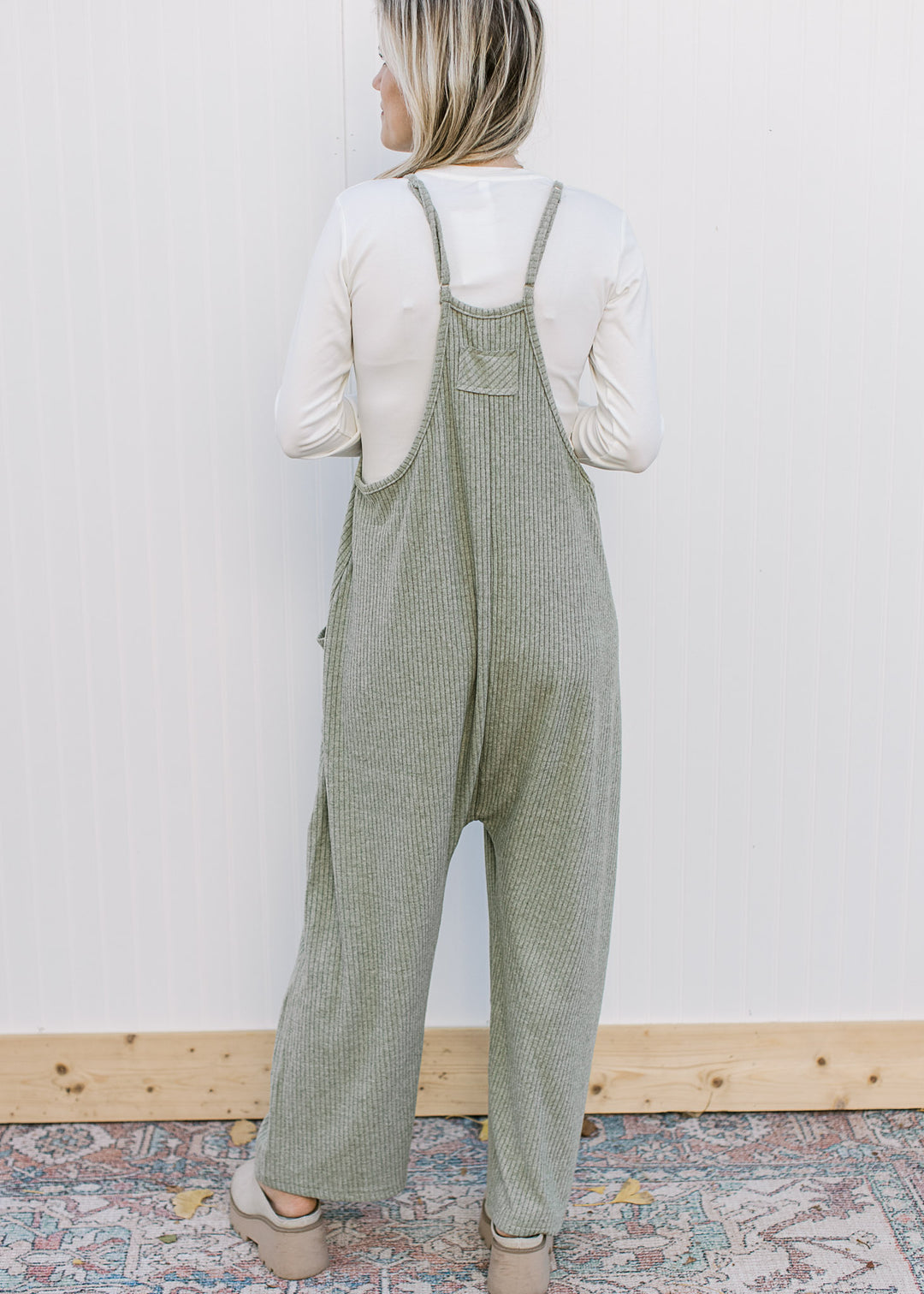 Back view of Model wearing a moss green ribbed jumper with adjustable straps and wide legs.