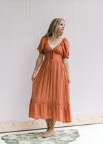 Model wearing a rust midi with bubble short sleeves a smocked band in back and a v-neck with a tie.