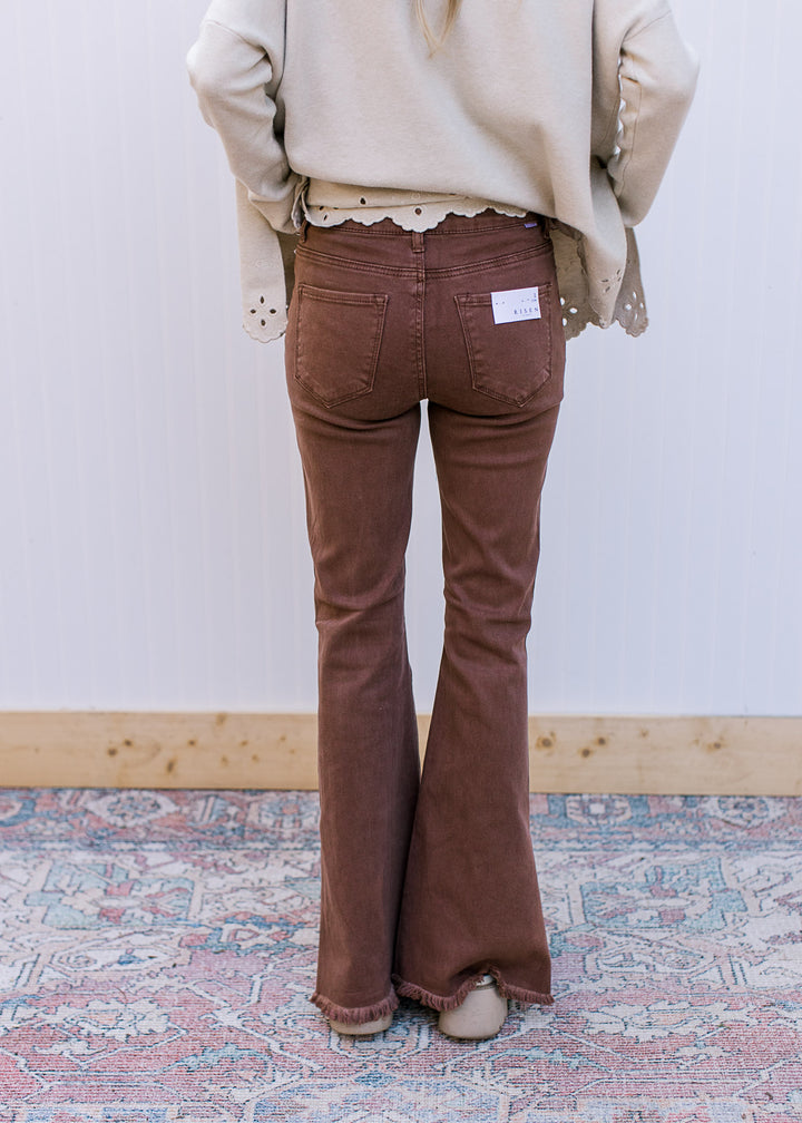 Back view of Model wearing espresso colored  jeans with side splits, raw hem and a flare leg.