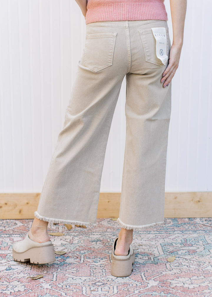 Back view of Model wearing khaki high rise jeans with a cropped fit, frayed hem and wide legs.