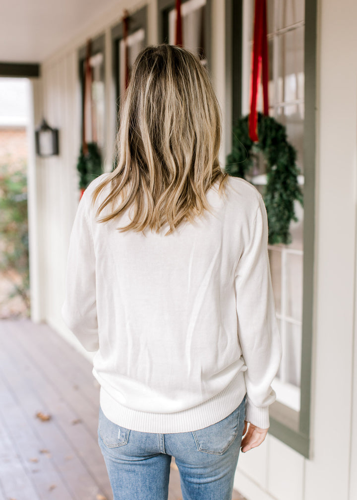 Back view of model wearing a white round neck sweater with holly jolly across the front.