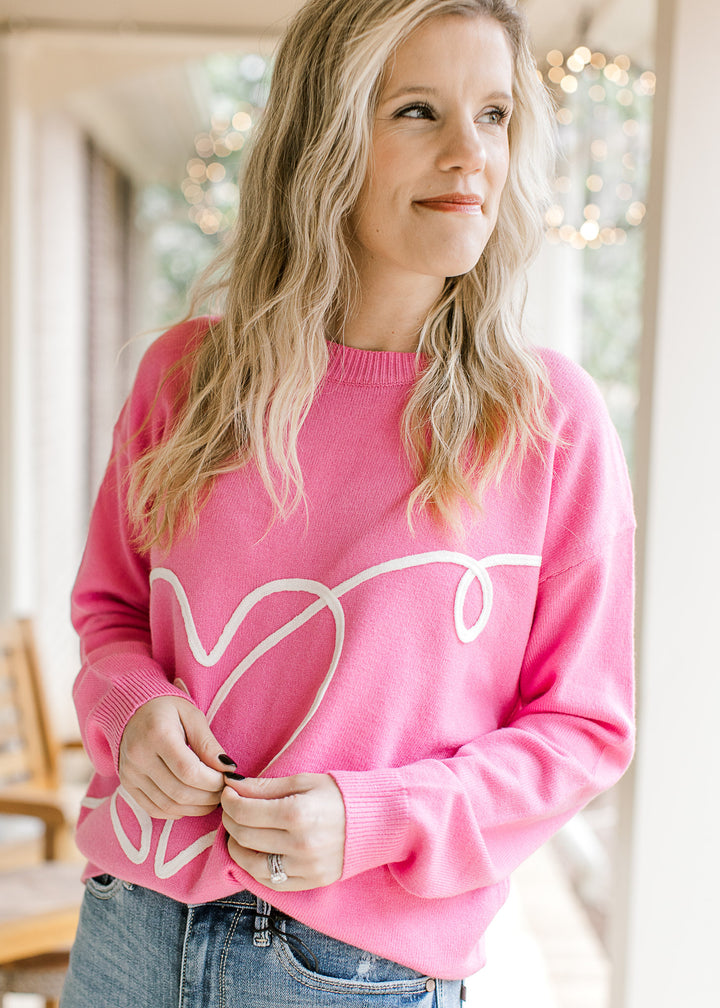 Model wearing a hot pink sweater with a cream heart design along the front and long sleeves.
