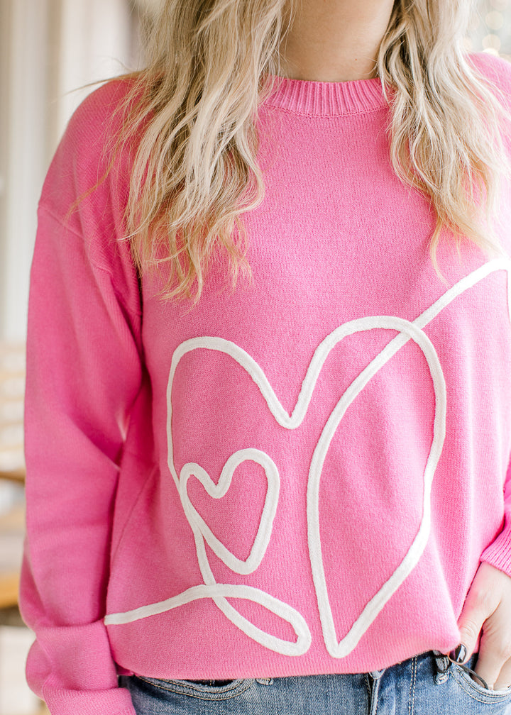 Close up of heart design in cream along the front of a hot pink sweater with long sleeves.