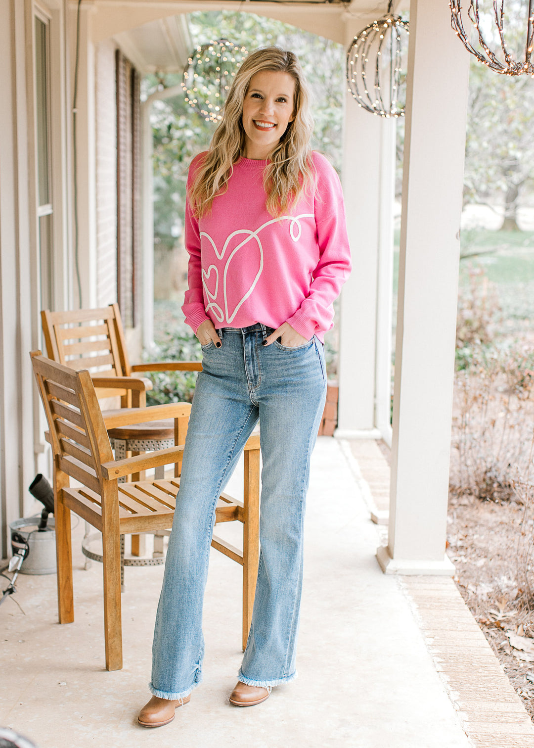 Model wearing jeans and a hot pink sweater with a cream heart design along the front.