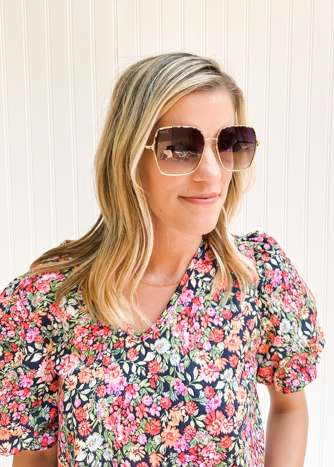 Model wearing sunglasses with a gold wire frame and gray ombré lenses with a floral top.