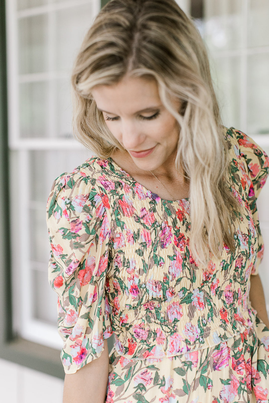 Close up of smocked bodice and short sleeves on a yellow dress with a pink and green floral.