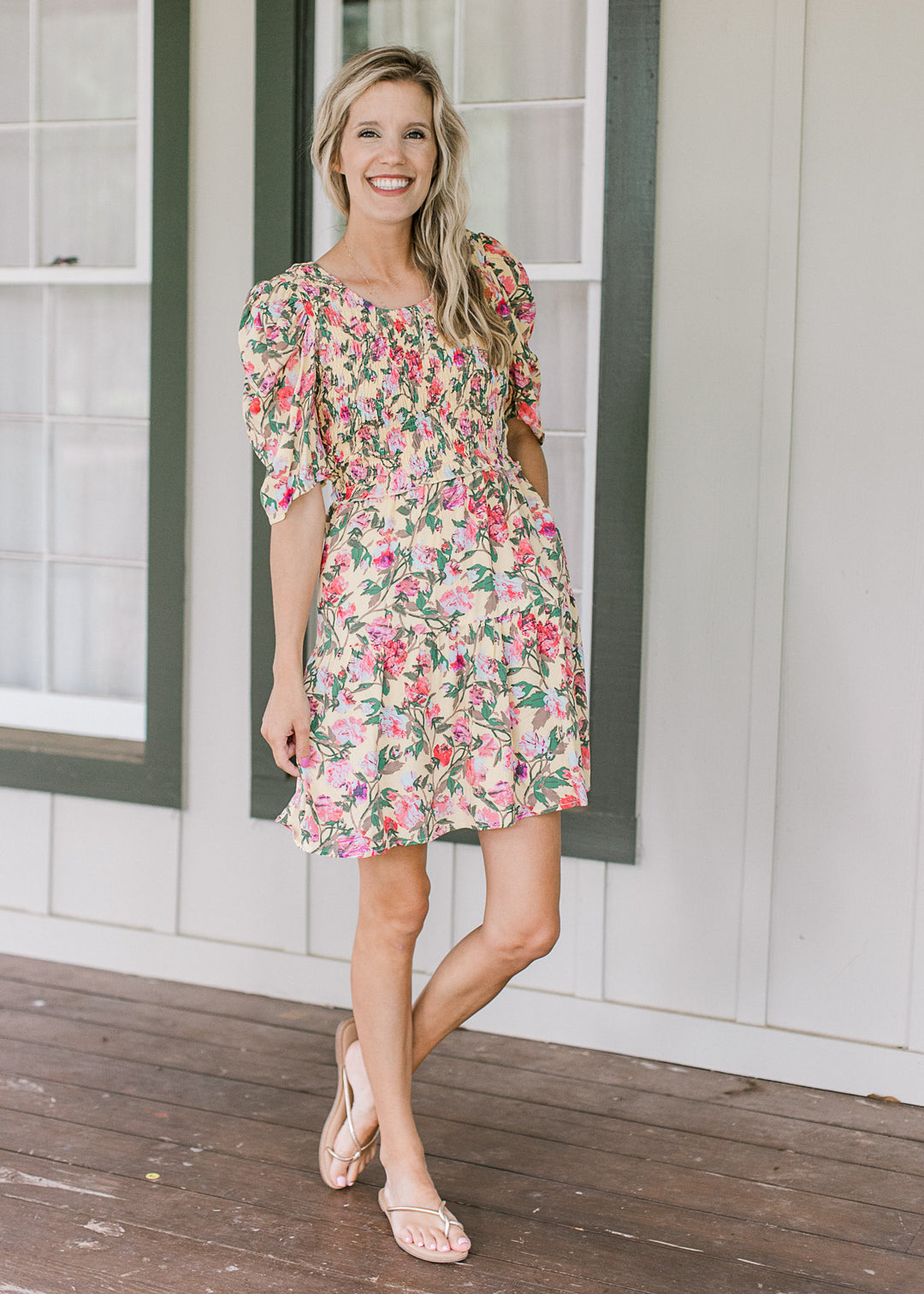 Model wearing sandals and a yellow dress with floral, smocked bodice and short sleeves.
