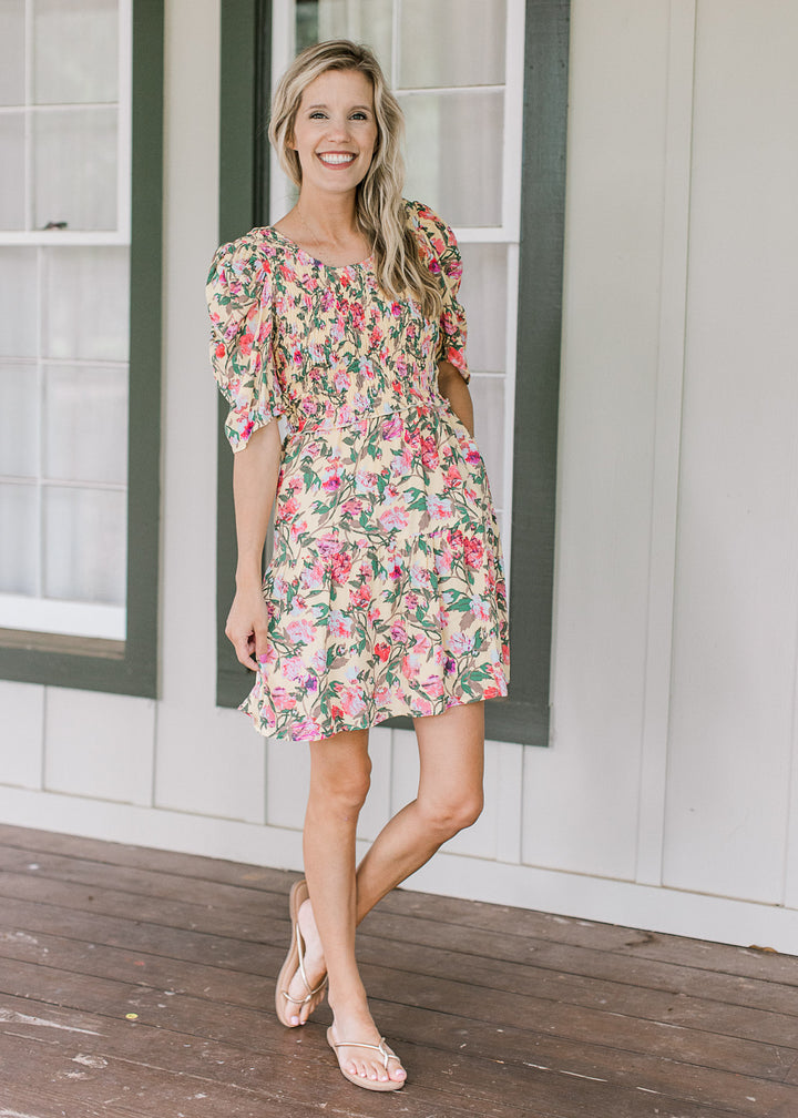 Model wearing sandals and a yellow dress with floral, smocked bodice and short sleeves.