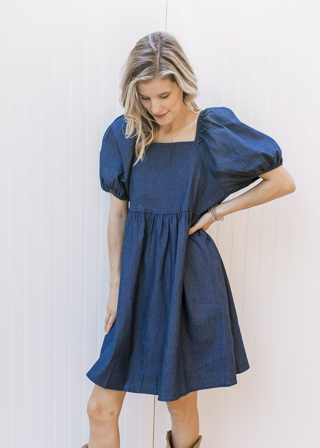 Model wearing an above the knee dress with a dark denim wash, square neck and bubble short sleeves.