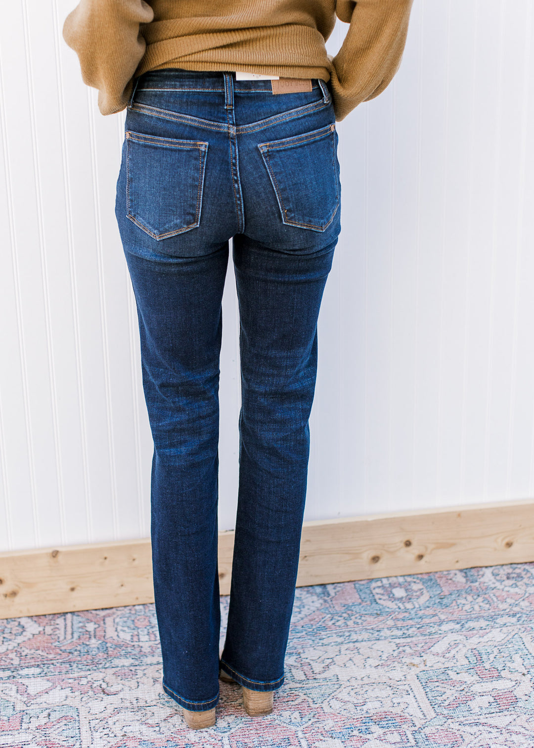 Back view of model wearing mid rise, dark wash jeans with a boot cut and stretchy fit.