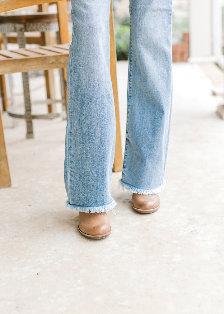 Close up of brown boots and frayed hem on medium washed bootcut jeans with high waistband.