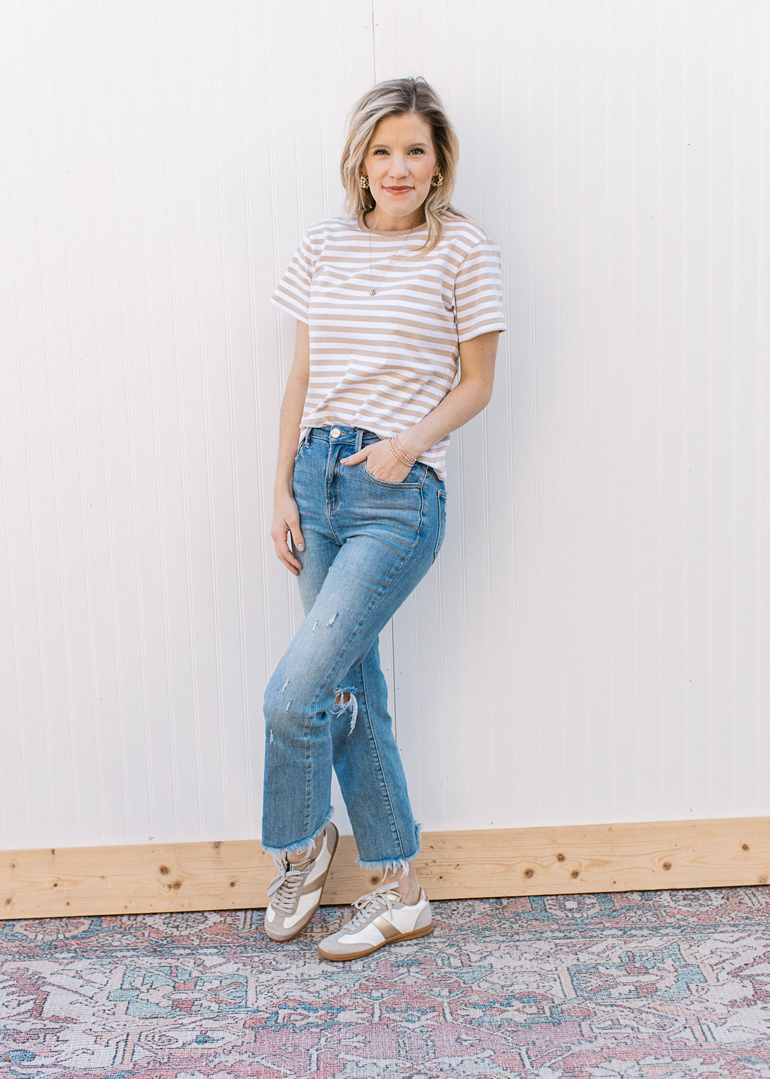 Model wearing jeans, sneakers and a white tee with khaki stripes, short sleeves and a crew neck.