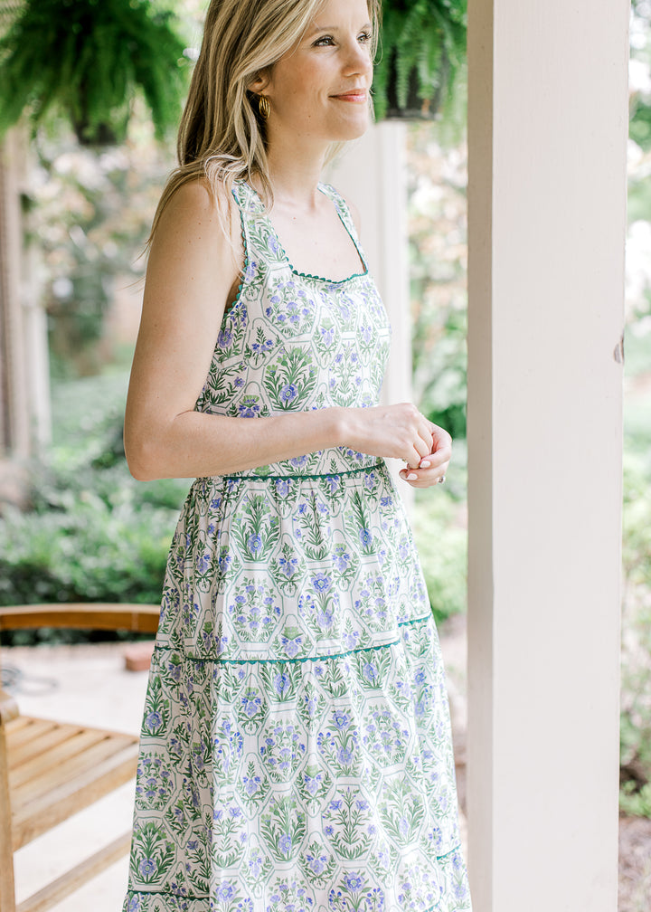 Model wearing a sleeveless white midi with green and blue floral, square neck, and elastic wasit.