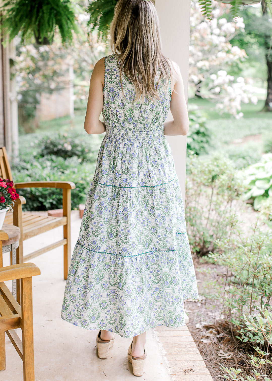 Back view of model wearing a sleeveless white midi with green and blue floral and elastic waist.