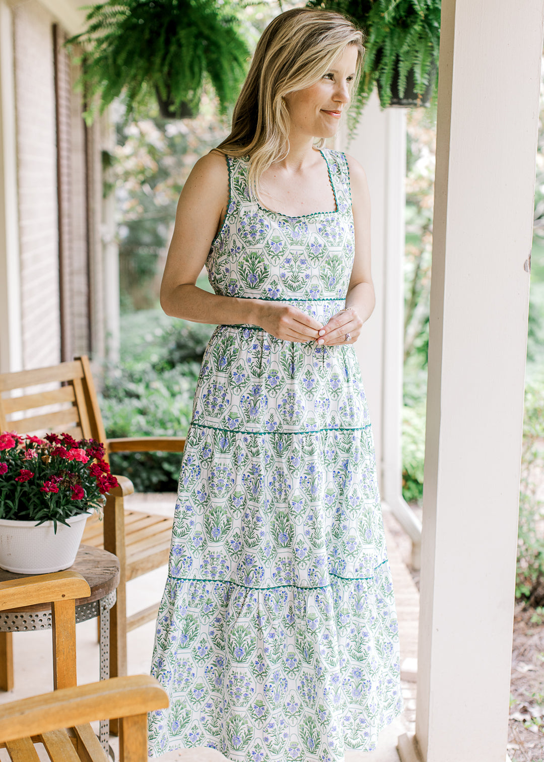 Model wearing a tiered sleeveless white midi with green and blue floral and a square neck.