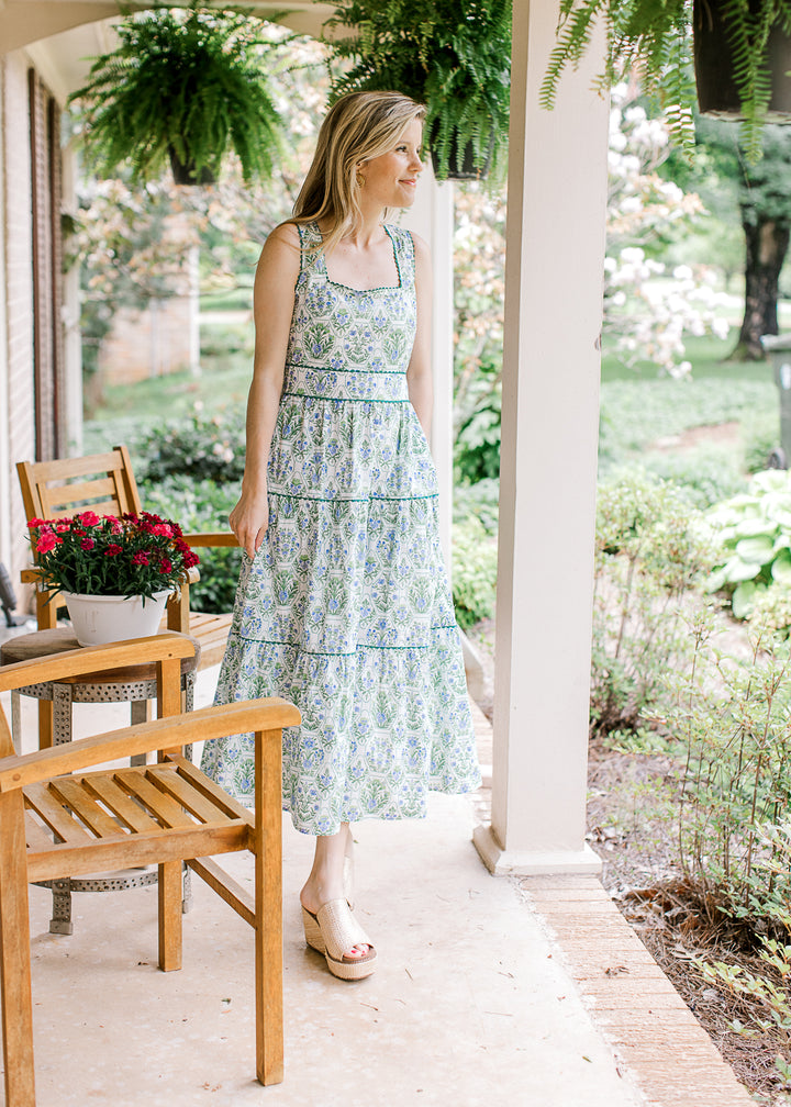 Model wearing wedges and a sleeveless white midi with green and blue floral and square neck.