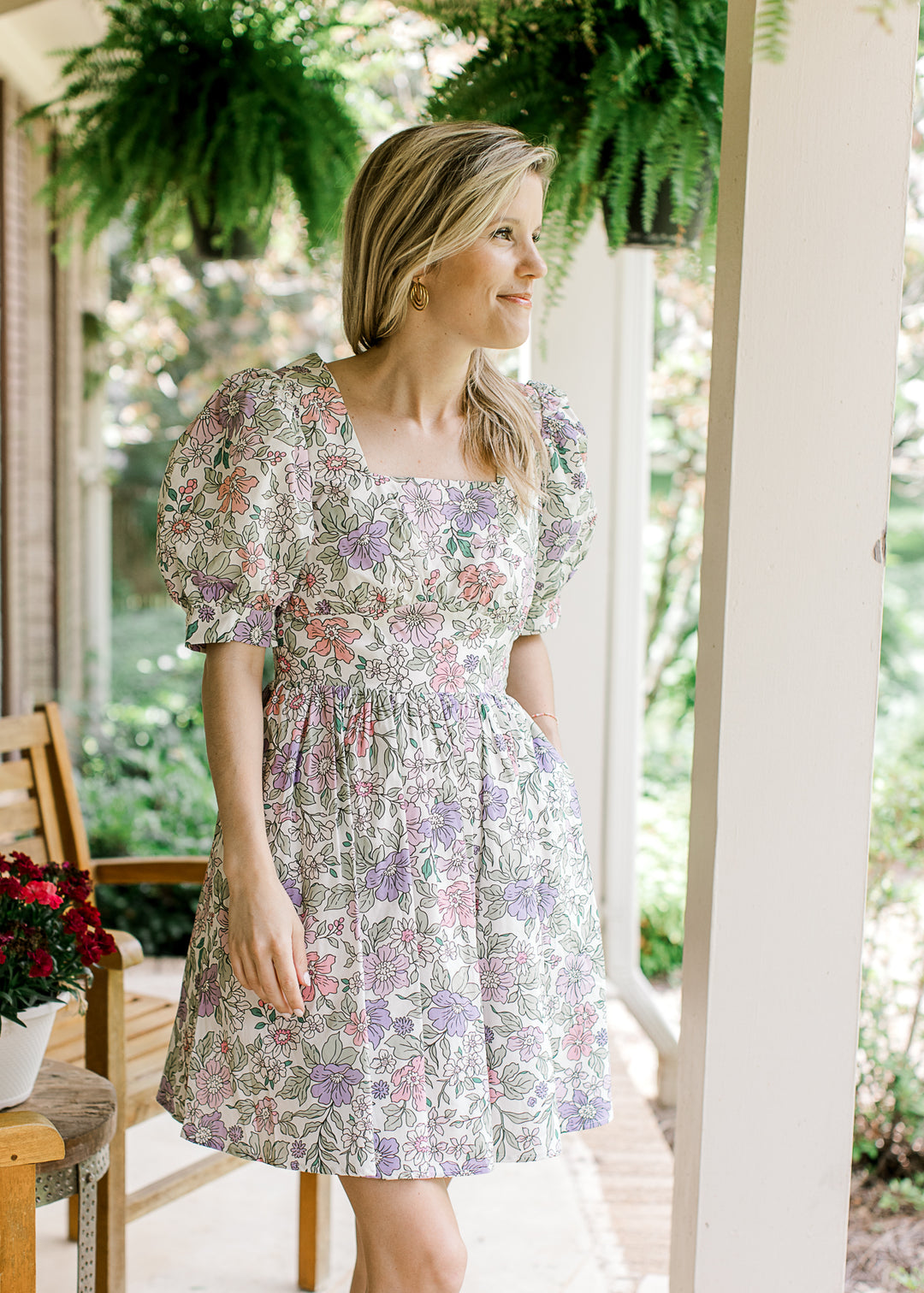 Model wearing a short sleeve, off white above the knee dress with pink, purple and green floral.