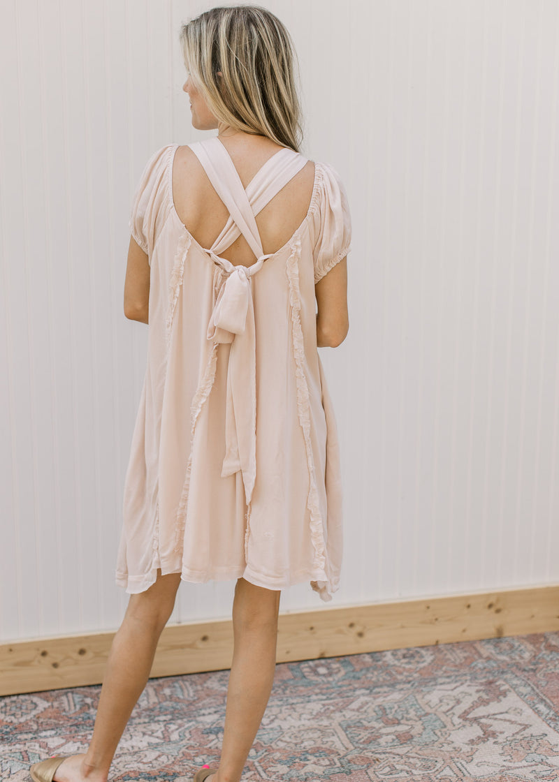Back view of a blush dress with cross back detail and an above the knee fit with a rayon material.