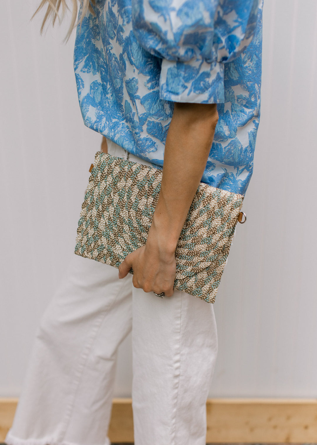 Model holding a gold, taupe, cream, and teal color lined purse with a snap closure.