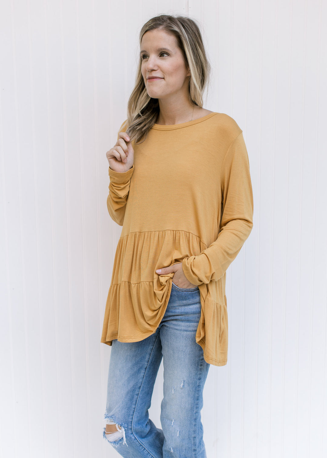 Model wearing a marigold, tiered top comprised of a bamboo material and long sleeves.