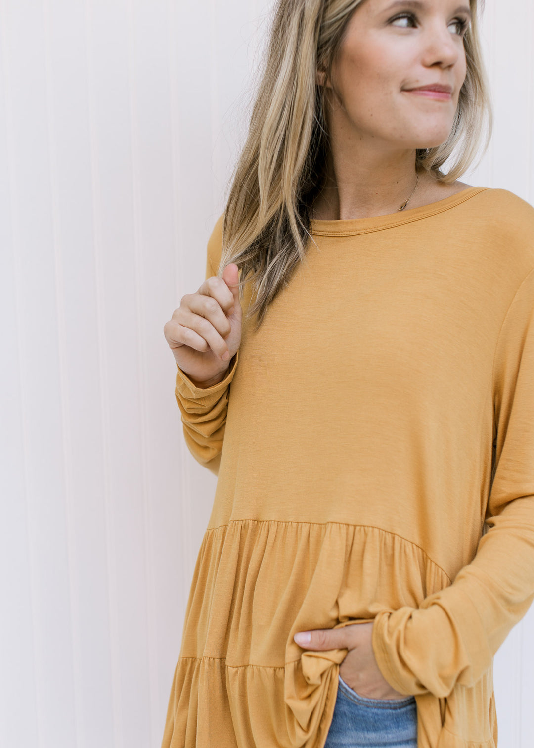 Close up of the tiers on a marigold colored top composed of a bamboo material with long sleeves.