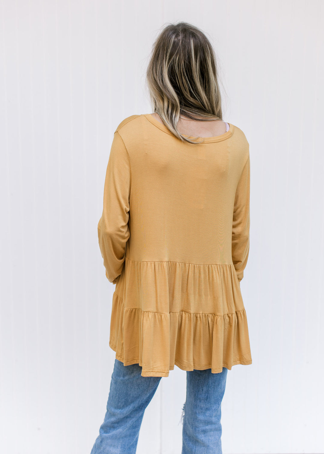 Back view of Model wearing a marigold, tiered top comprised of a bamboo material and long sleeves.
