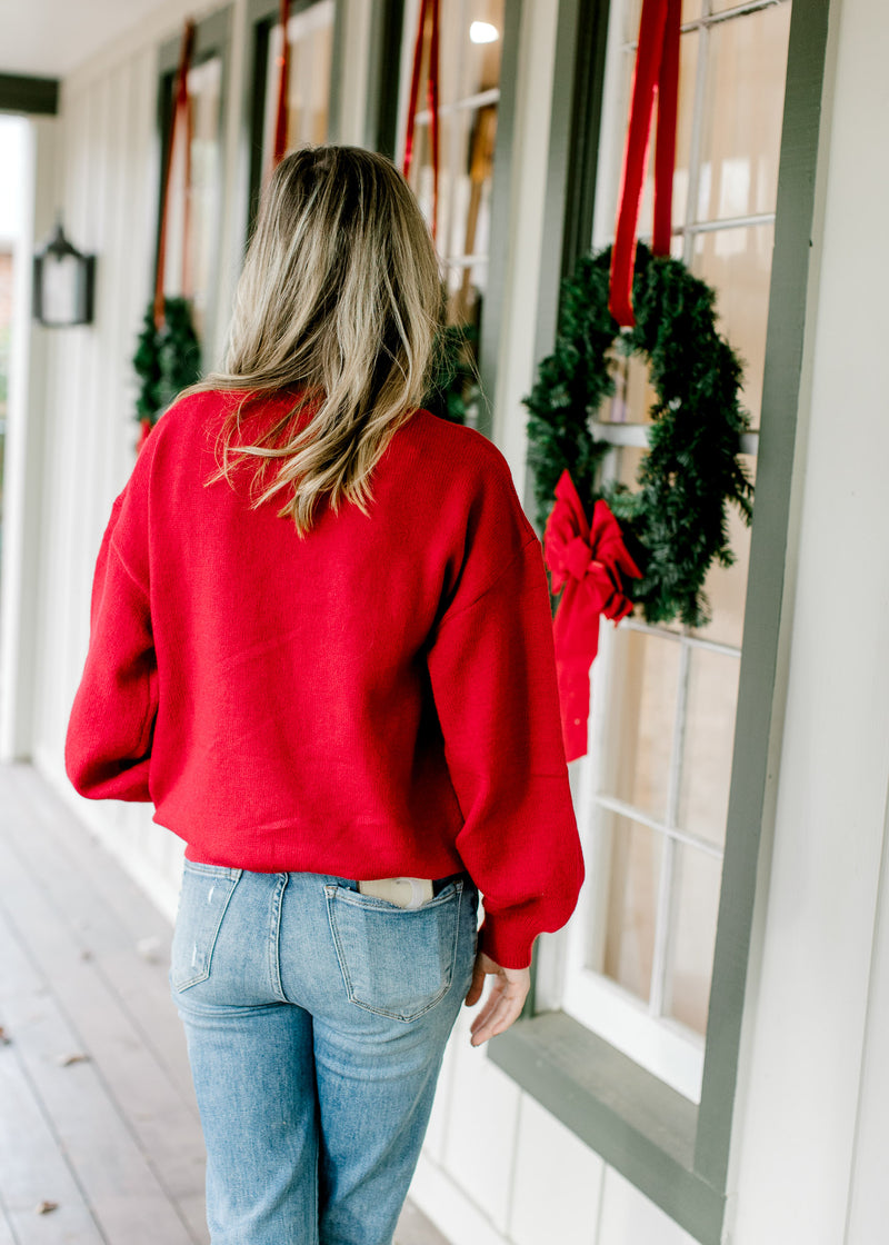 Back view of Model wearing a red long sleeve sweater with merry scripted in white across the front. 