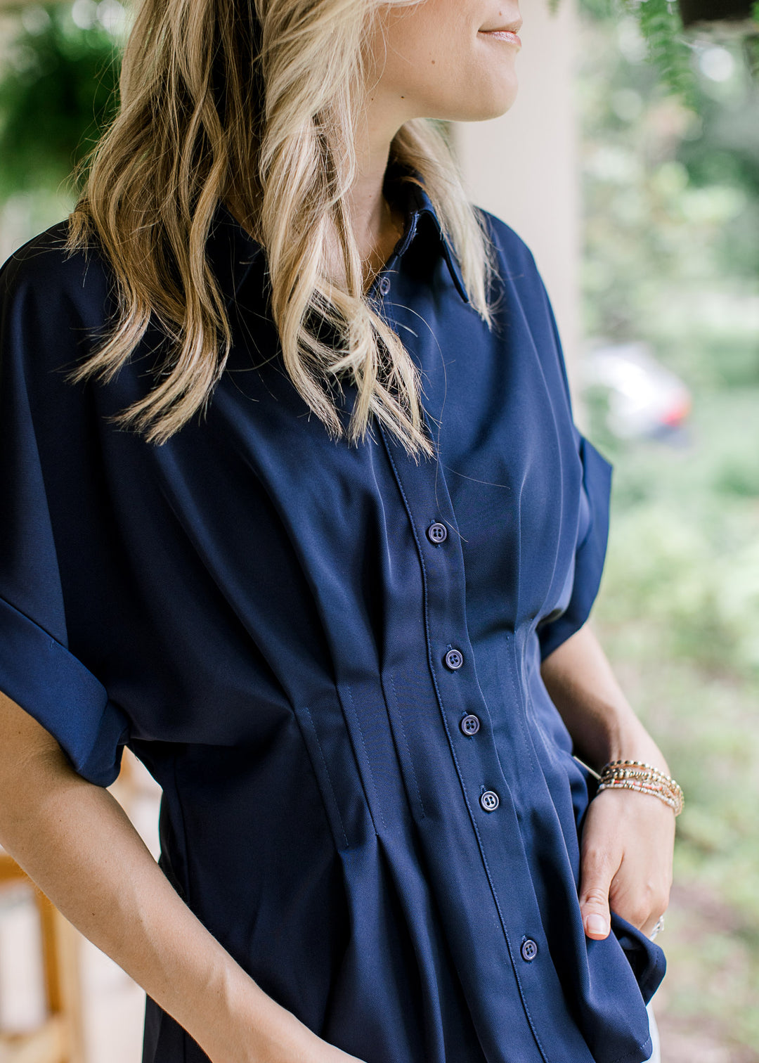 Model wearing a navy top with cuffed short drop shoulder sleeves, buttons and a pleated waist.