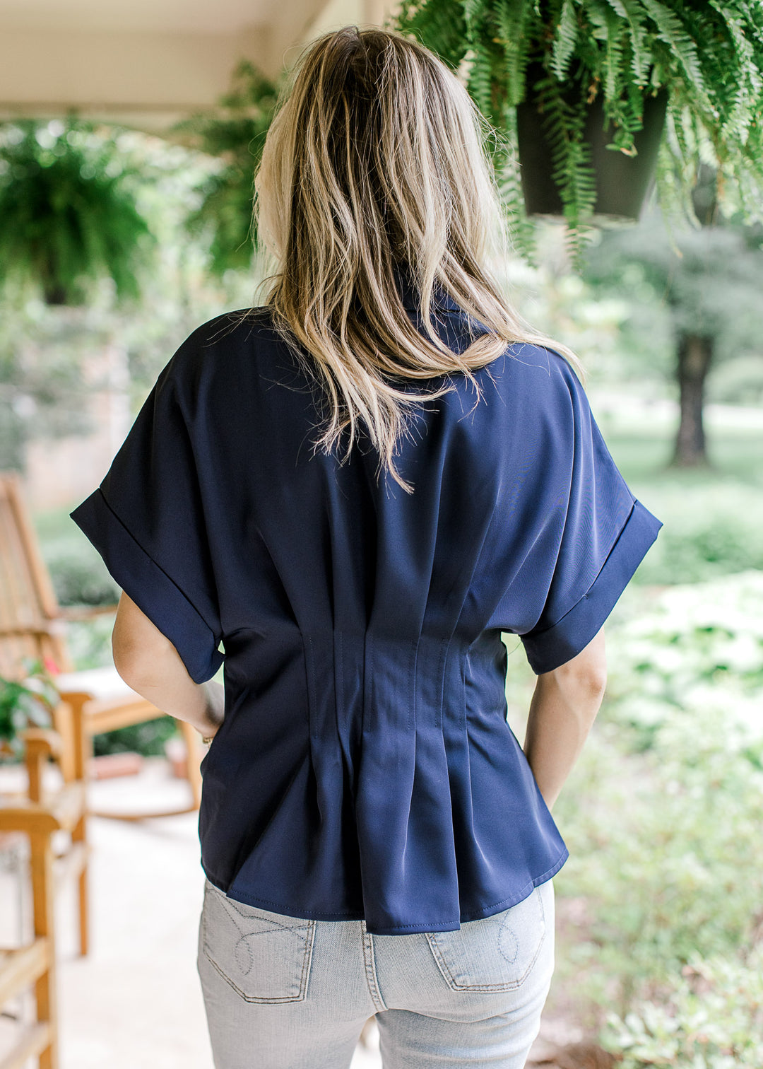 Back view of Model wearing a navy top with cuffed short drop shoulder sleeves and a pleated waist.