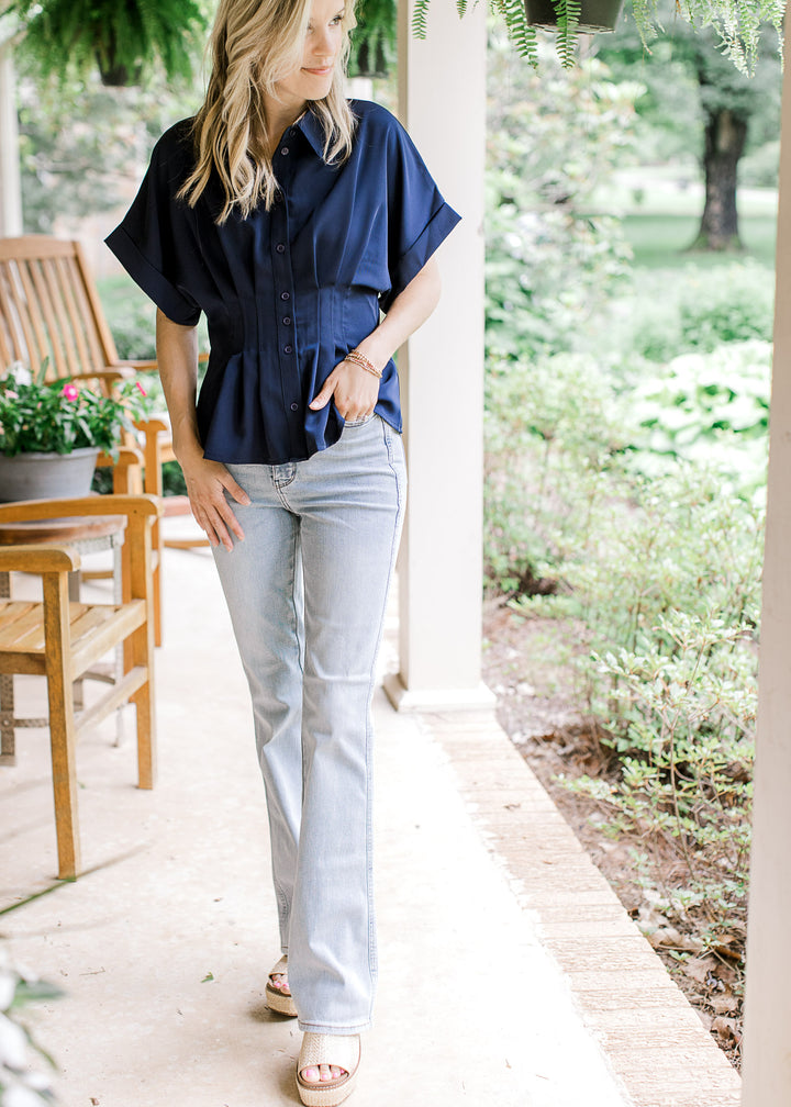 Model wearing jeans and a navy top with cuffed short sleeves, buttons and a pleated waist.