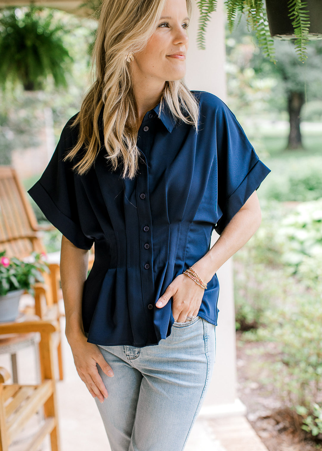 Model wearing a navy top with cuffed drop shoulder sleeves, buttons and a pleated waist.