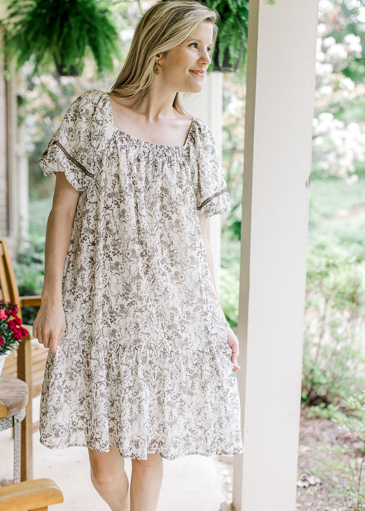 Model wearing a cream short sleeve, above the knee dress with mocha floral and square neck.