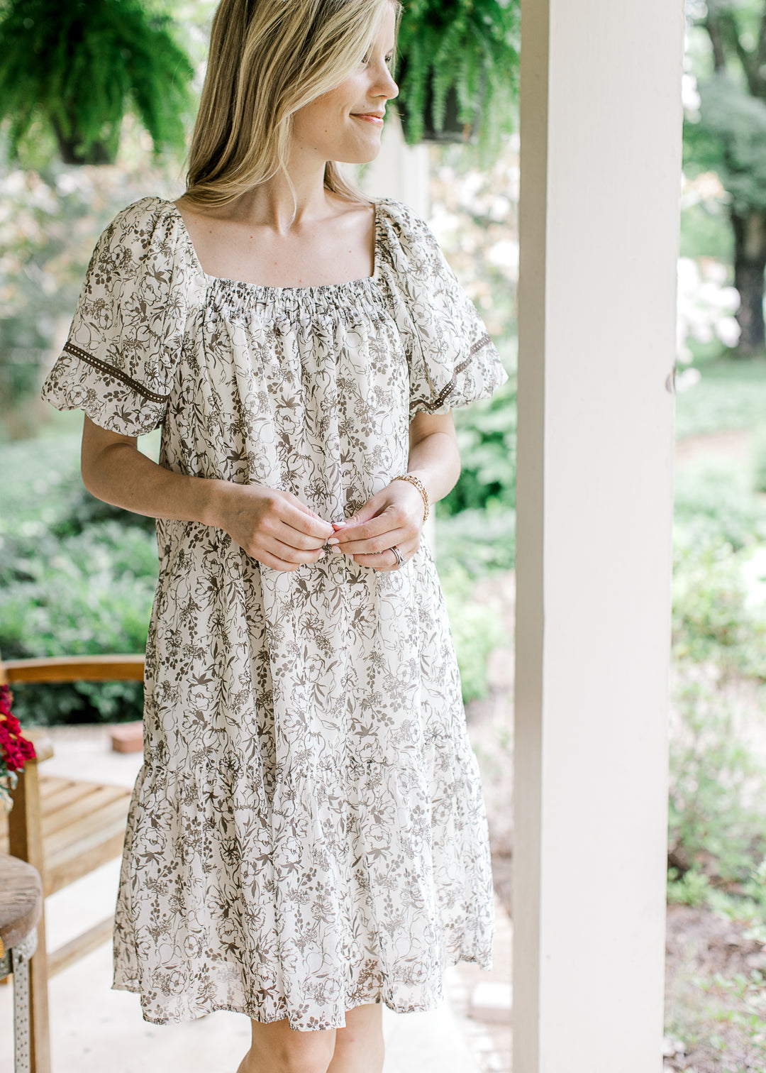 Model wearing a cream short sleeve, dress with mocha floral and square neck with smocking.