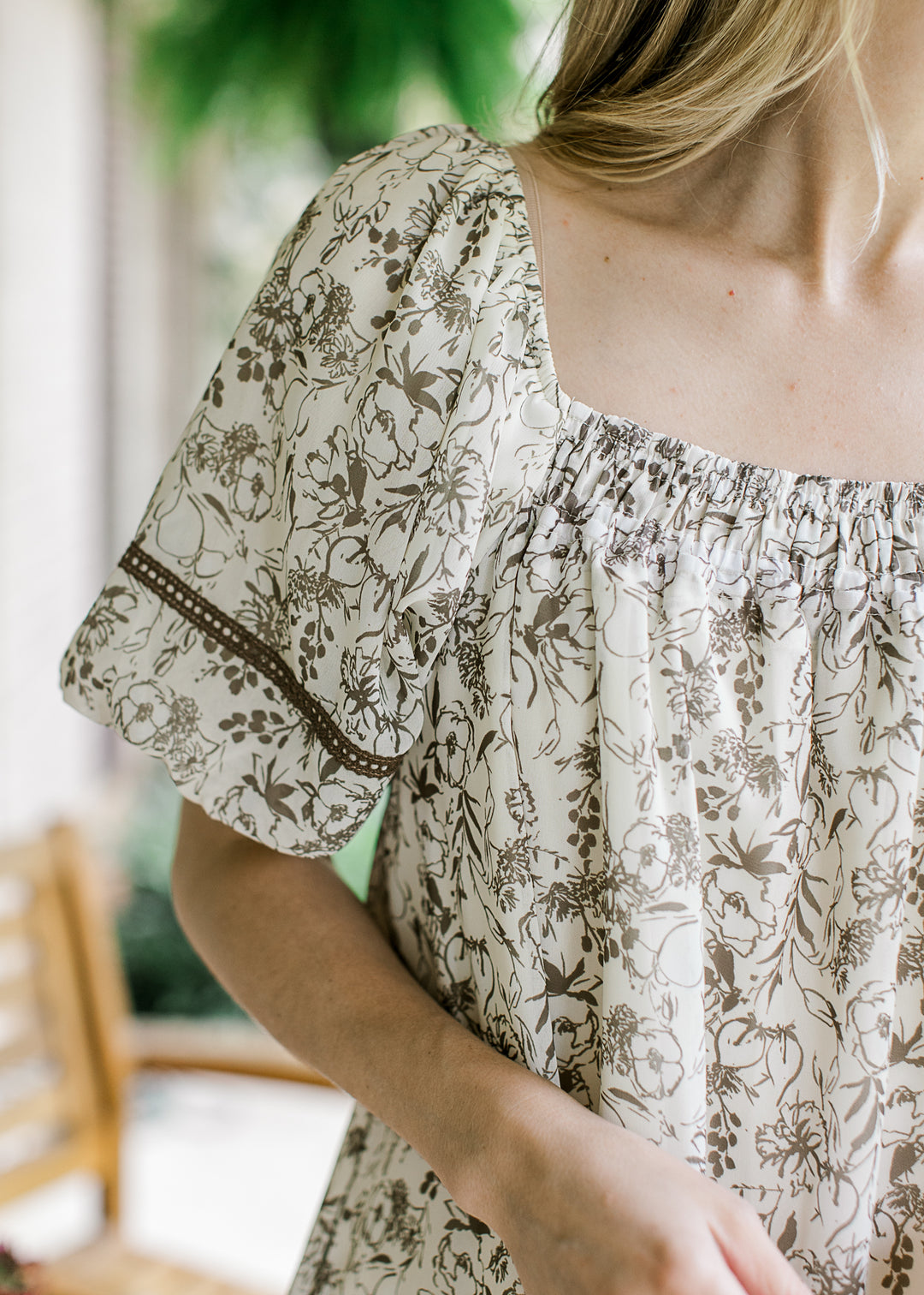Close up of bubble short sleeve and square neck with smocking on a cream dress with flowers.