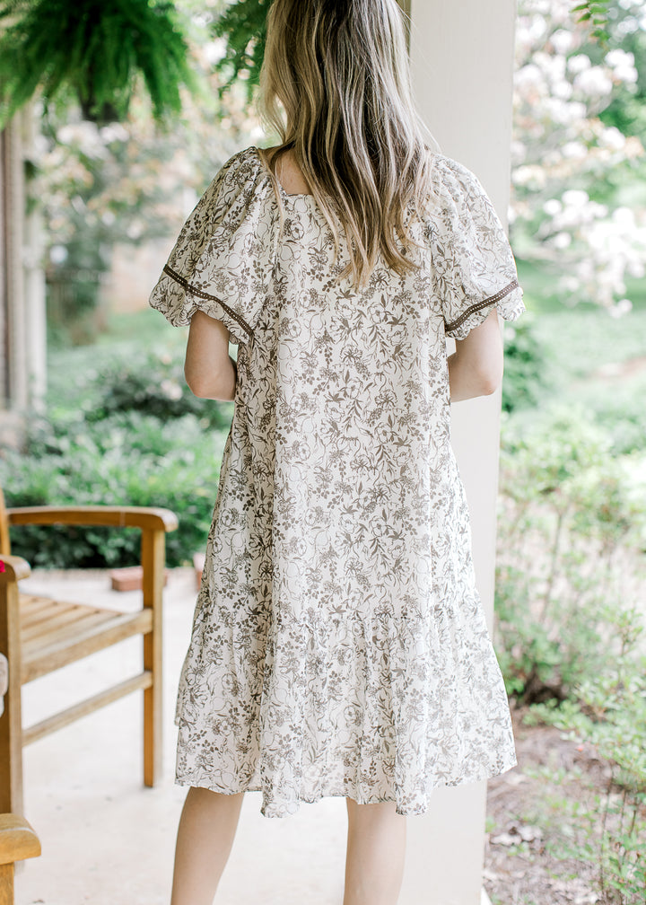 Back view of Model wearing a cream short sleeve dress with mocha floral and square neck.