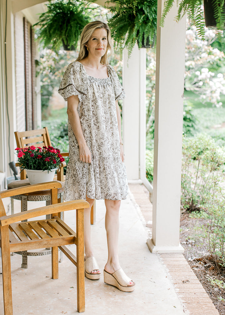 Model wearing wedges and a cream short sleeve dress with mocha floral and square neck.