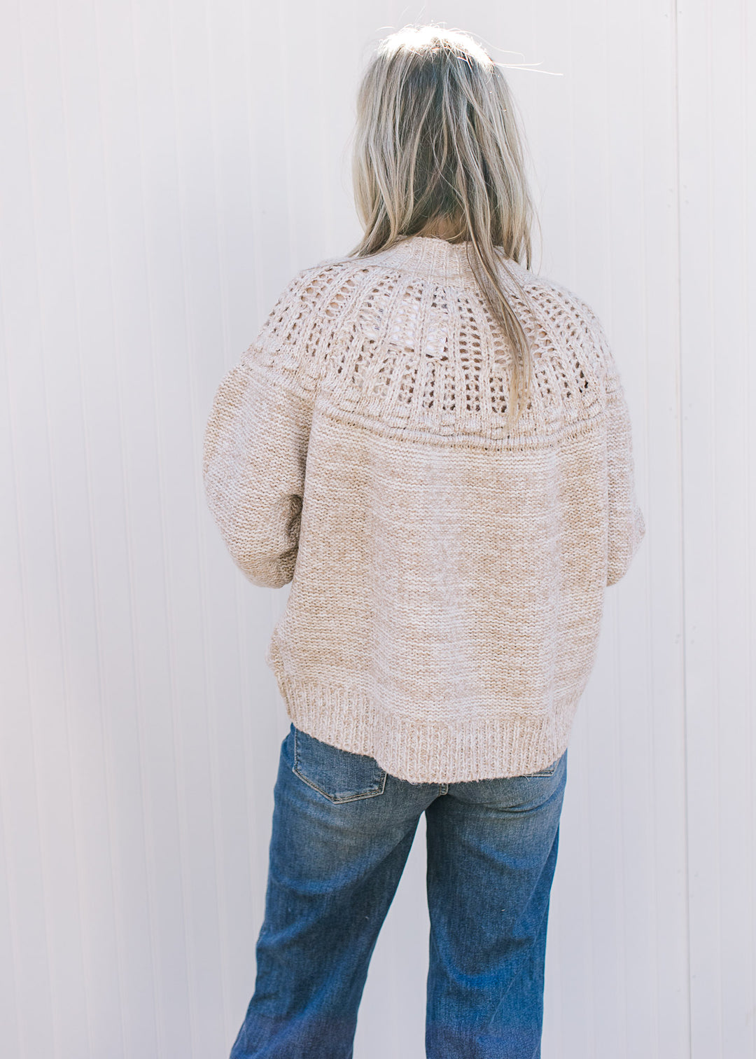 Back view of Model wearing an oatmeal colored sweater with open knit yolk detail and a mock neck.