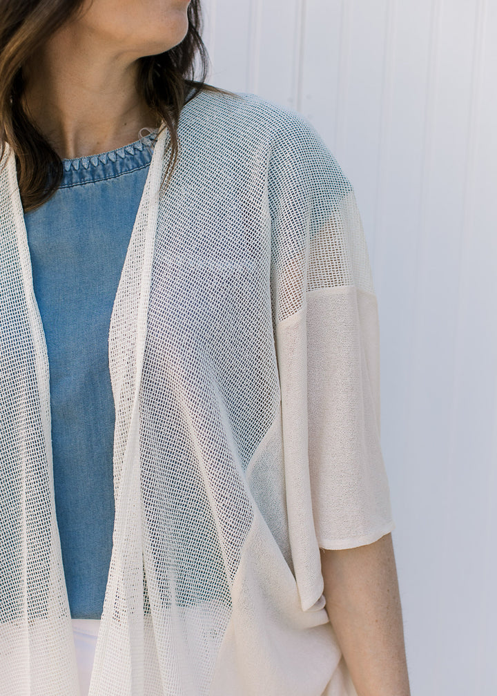 Model wearing a cream, maxi length duster with a sheer woven fabric with light knit inset.