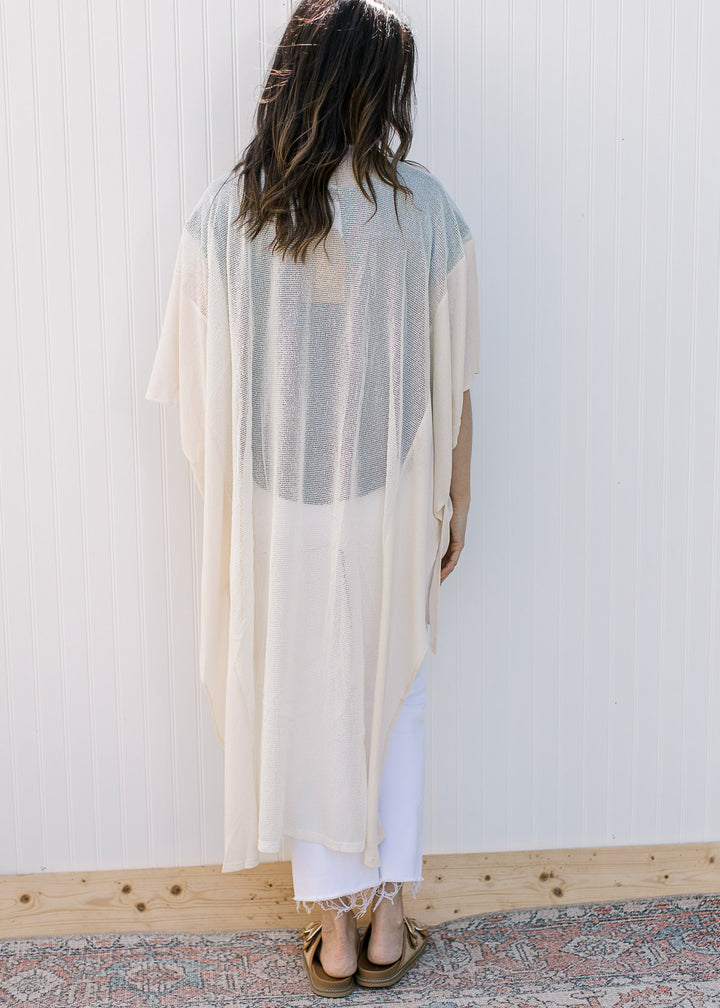 Back view of Model wearing a cream, maxi length duster with a sheer woven fabric with knit inset.